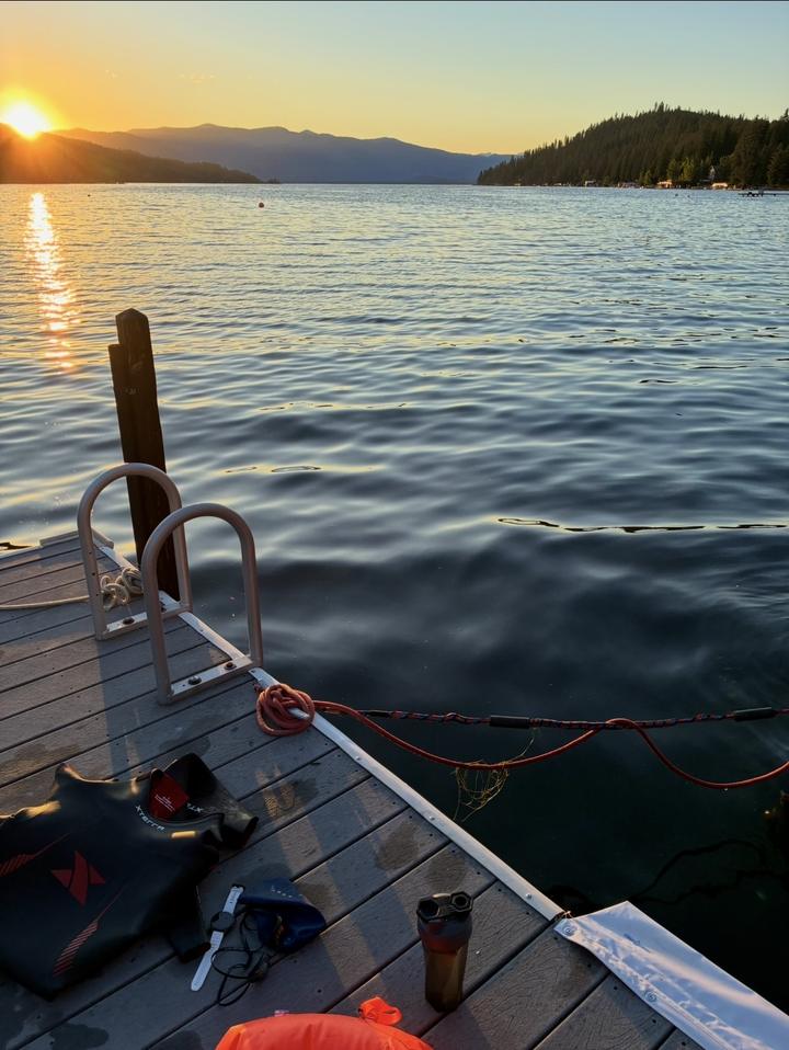 Wetsuit, goggles, watch and swim buoy on a dock at sunrise